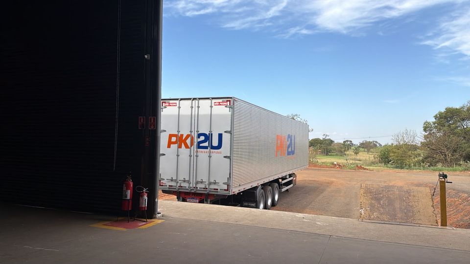 Carreta baú branca com a marca PK2U encostada na doca do galpão da matriz